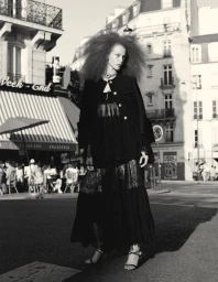 Model standing on a city street wearing a black jacket and long dress with voluminous curly hair