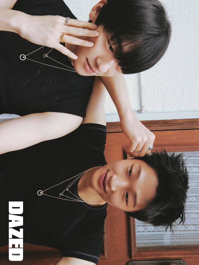 Two young Asian men with short dark hair wear black shirts and silver necklaces. They pose indoors with soft lighting and jewelry.