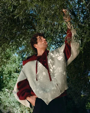 Man in textured knit cardigan reaching up into olive tree branches for GQ Mexico