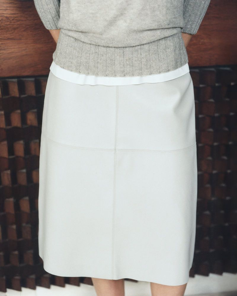 A-line leather skirt in a neutral tone paired with a cozy grey sweater, creating a minimalist and fashionable indoor aesthetic.