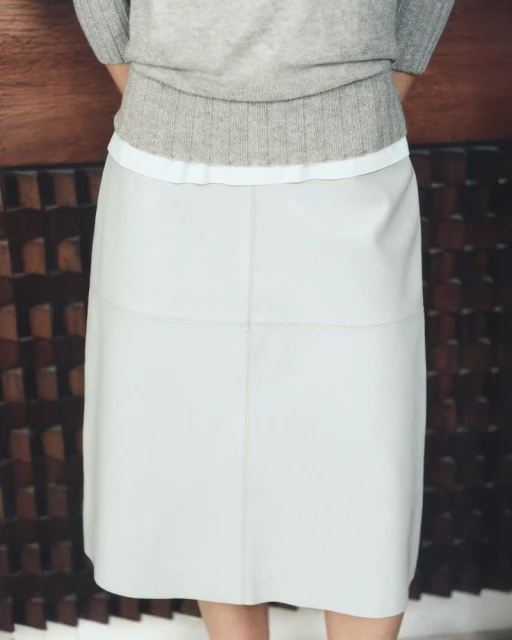 A-line leather skirt in a neutral tone paired with a cozy grey sweater, creating a minimalist and fashionable indoor aesthetic.