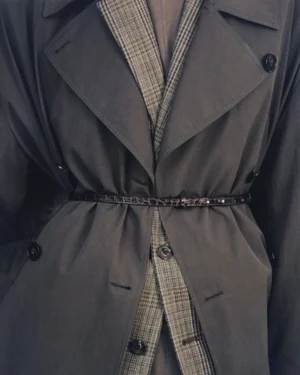 Close-up of a belted charcoal grey trench coat layered over a brown plaid blazer with dark buttons.
