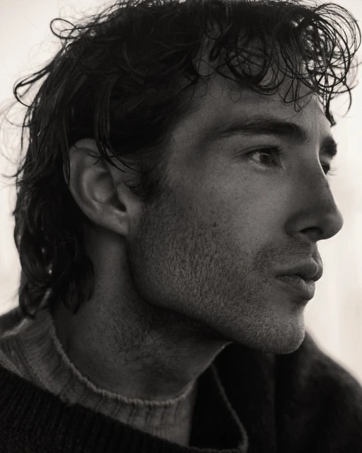 Monochrome portrait of a man in profile, captured in a close-up shot showcasing his dark hair and a crewneck sweater.