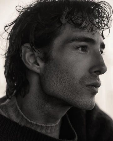 Monochrome portrait of a man in profile, captured in a close-up shot showcasing his dark hair and a crewneck sweater.