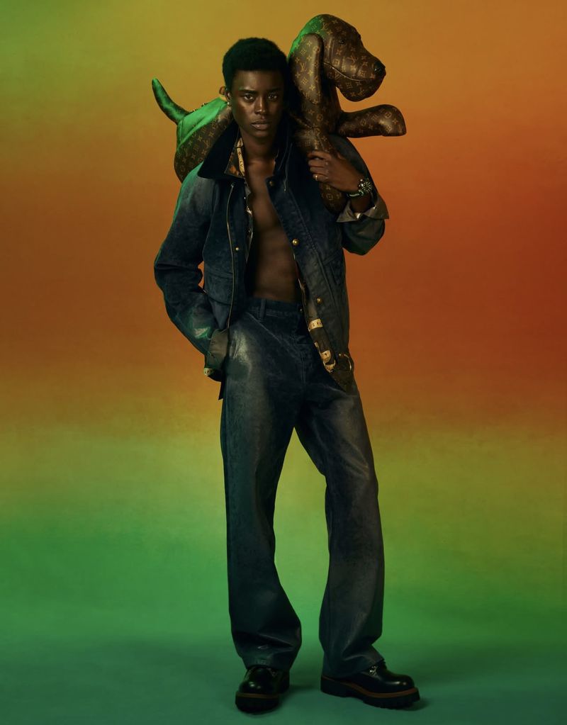 A fashionable young Black man strikes a pose with a brown, patterned inflatable dog. His denim jacket and pants add a chic touch.