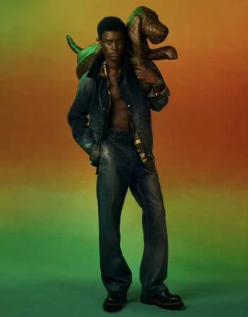 A fashionable young Black man strikes a pose with a brown, patterned inflatable dog. His denim jacket and pants add a chic touch.