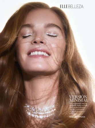 Beauty shot of a woman with light brown hair smiling with her eyes closed and wearing glittery eye makeup and a diamond necklace.