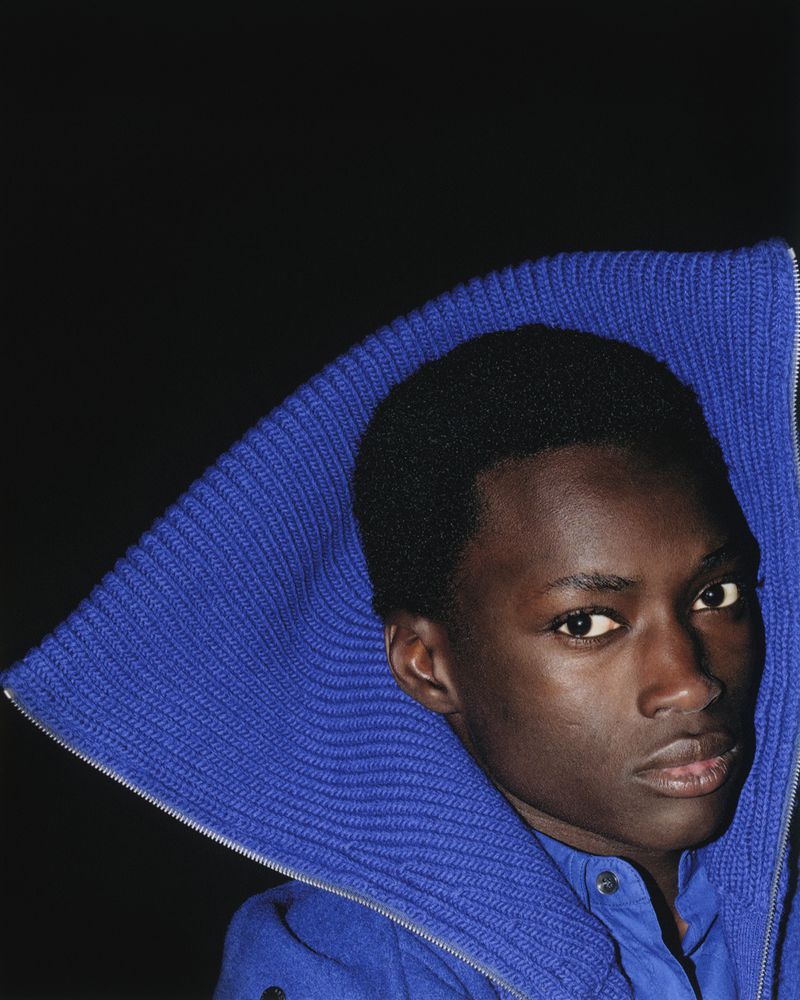 Close-up portrait of a young African American male in blue jacket against a dark background, showcasing textures and fashion details.