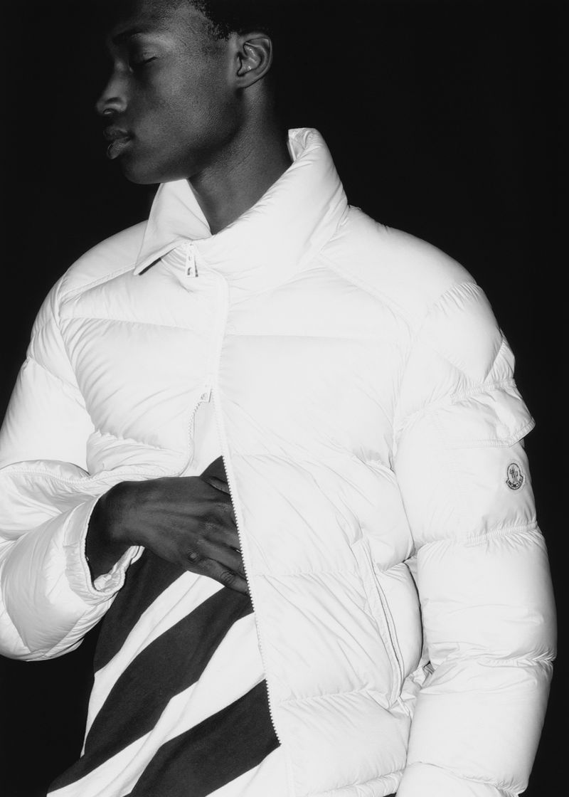 Monochromatic fashion shot of a Black male model wearing a white puffer jacket with black and white striped shirt in a studio setting.