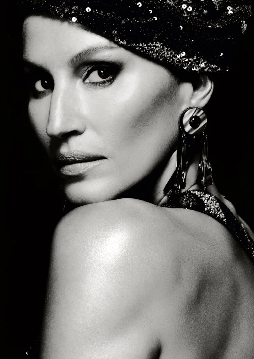 Monochrome portrait of a woman with a sequined beret and dangling earrings, gazing over her shoulder against a dark background.