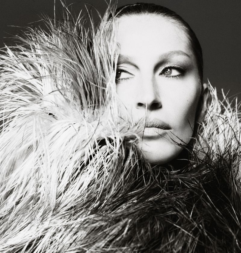 Black and white portrait of a woman with neutral expression, framed by feathers, eyes glancing to the side.