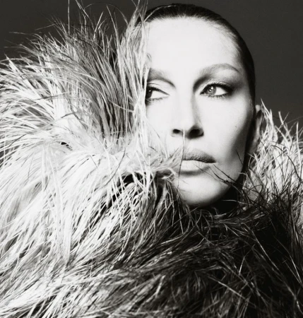 Black and white portrait of a woman with neutral expression, framed by feathers, eyes glancing to the side.