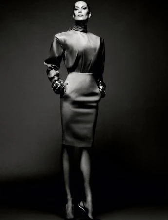 Elegant full-length portrait of an adult woman in a satin high-neck blouse, pencil skirt, and chunky jewelry against a gray backdrop.