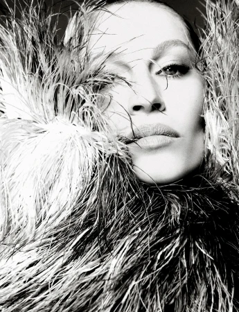Monochromatic portrait of a person framed by dark and light feathers, gazing directly at the camera with a serious expression.