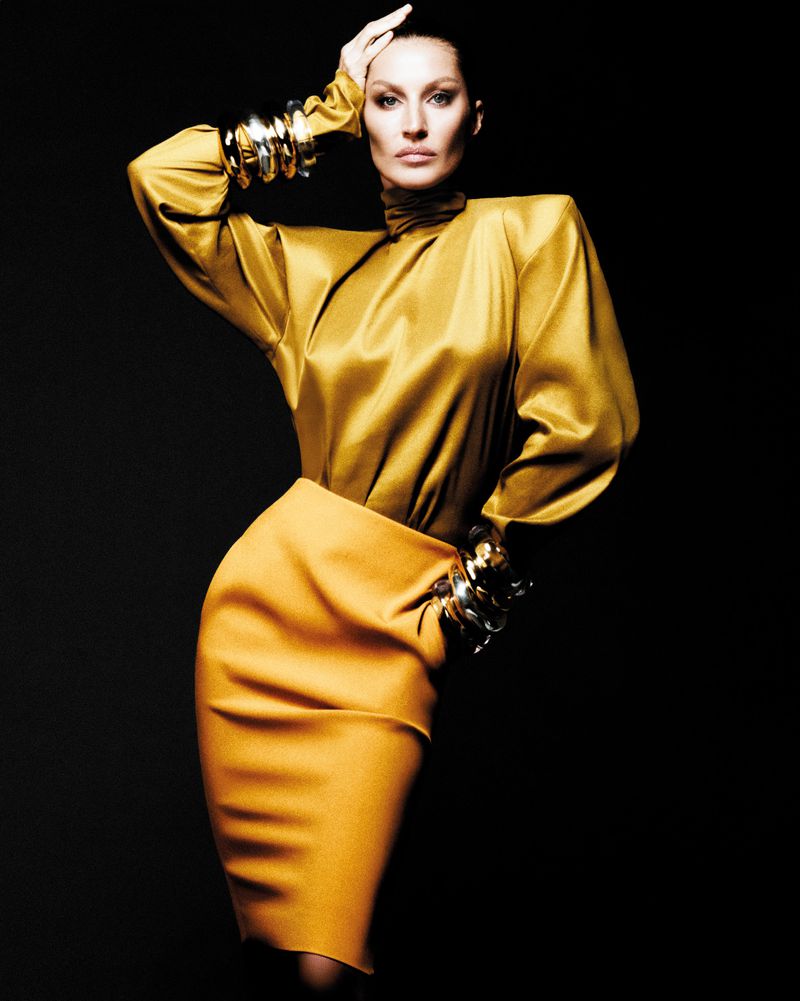 A poised model showcases a gold satin blouse and mustard skirt against a dark backdrop, adorned with silver cuff bracelets on her wrists.