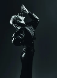 Model Hannah Motler in a black leather jacket tilts her head back holding an ornate bottle against a dark background.