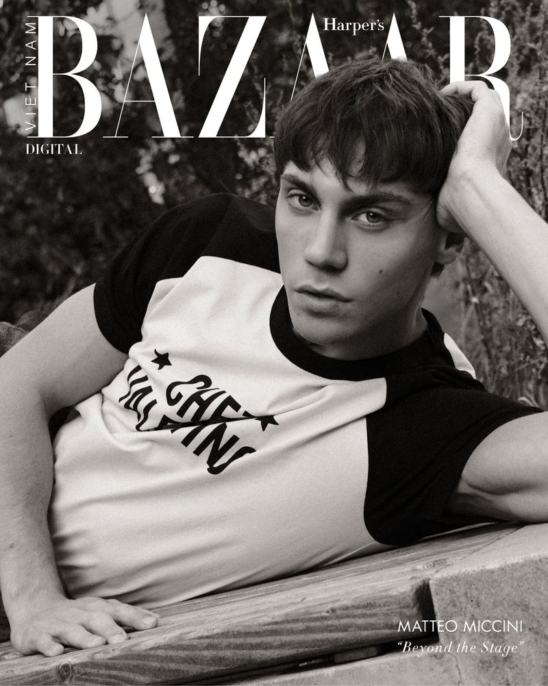 Black and white portrait of a young man lying on wooden planks in front of foliage, fashion editorial for Harper's Bazaar Vietnam.