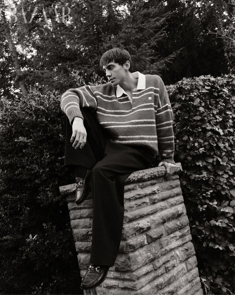 Matteo Miccini sitting on a stone pillar wearing a striped polo sweater and dark trousers for Harper's Bazaar Vietnam.
