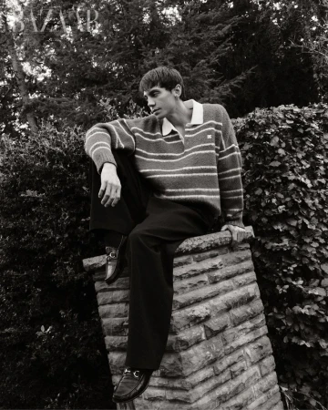 Matteo Miccini sitting on a stone pillar wearing a striped polo sweater and dark trousers for Harper's Bazaar Vietnam.