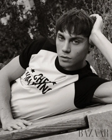 Matteo Miccini reclining outdoors on a wooden surface, resting his head on his hand while wearing a two-tone raglan t-shirt.