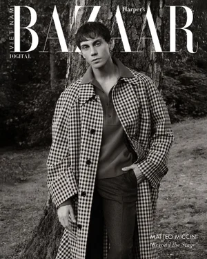 Matteo Miccini wearing a checkered overcoat and polo shirt while leaning against a tree in a woodland setting.