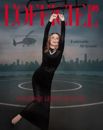 Philippine Leroy-Beaulieu in a sheer striped black maxi dress hanging from helicopter landing gear on a rooftop helipad.