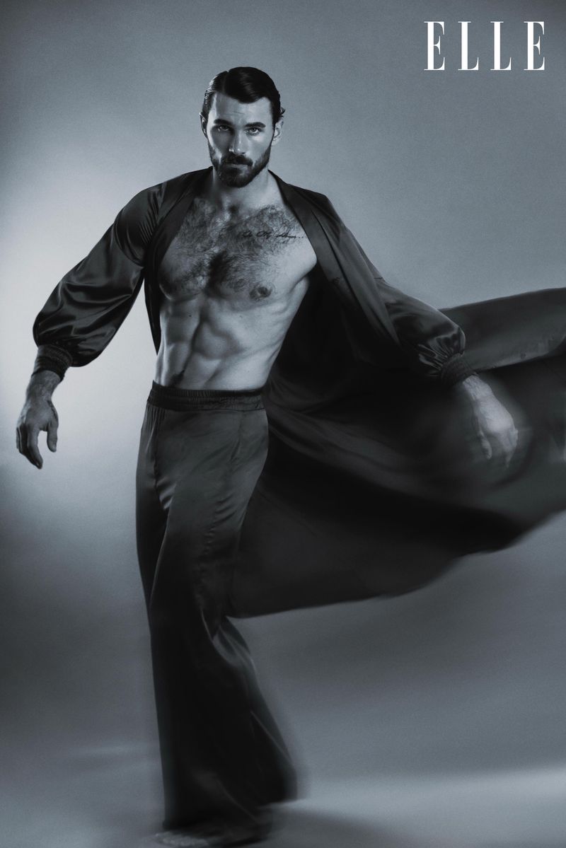 Athletic male fashion model poses shirtless wearing robe and pants in a studio lit monochromatic fashion editorial for Elle magazine.