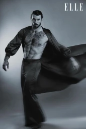 Model Michael Yerger posing shirtless in flowing dark silk trousers and an open robe in a black-and-white studio editorial.