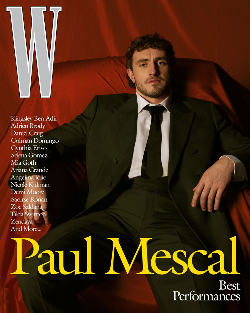 Paul Mescal in a suit, featured on the cover of W magazine. Actor shown sitting on a reddish-orange draped surface. Shot in a photo studio.