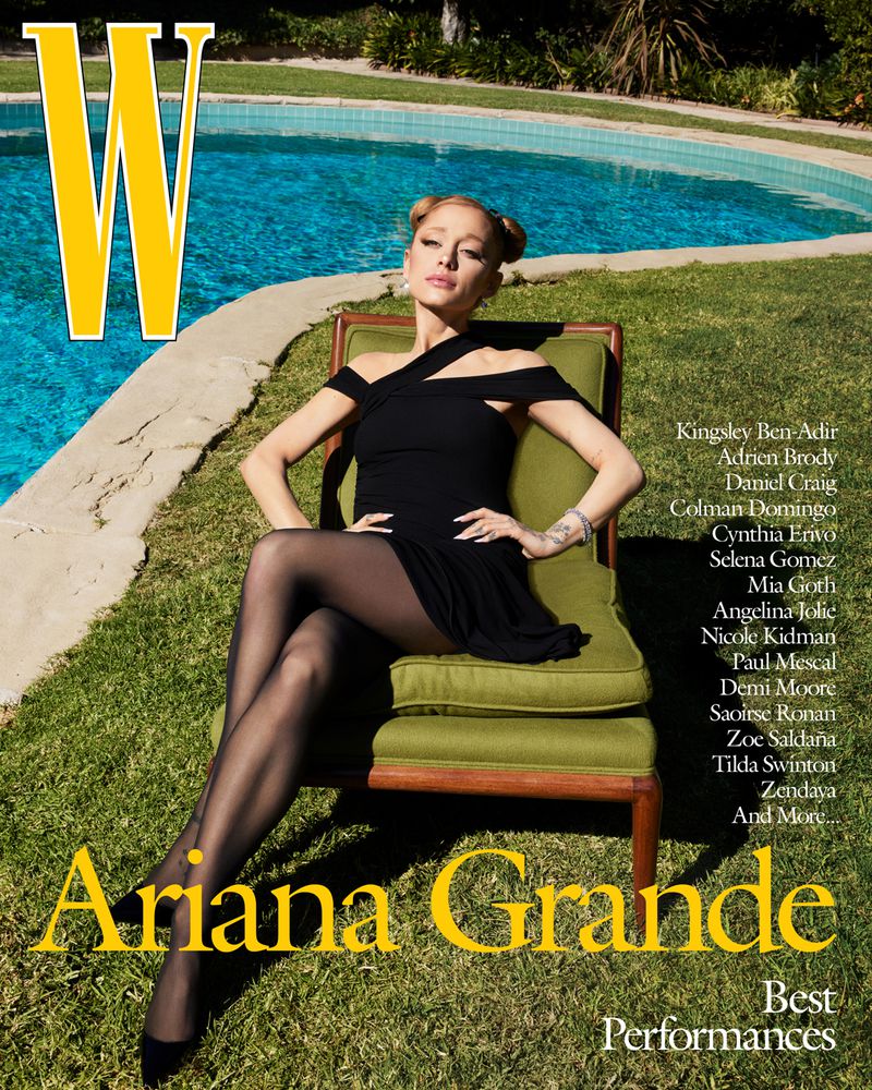 Ariana Grande sits on an olive chair in a black dress with black tights in front of a pool with green trees and grass in the background.