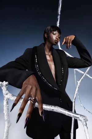 Black female model posing in an open black blazer with embellished lapels among silver branches for Numero Netherlands.