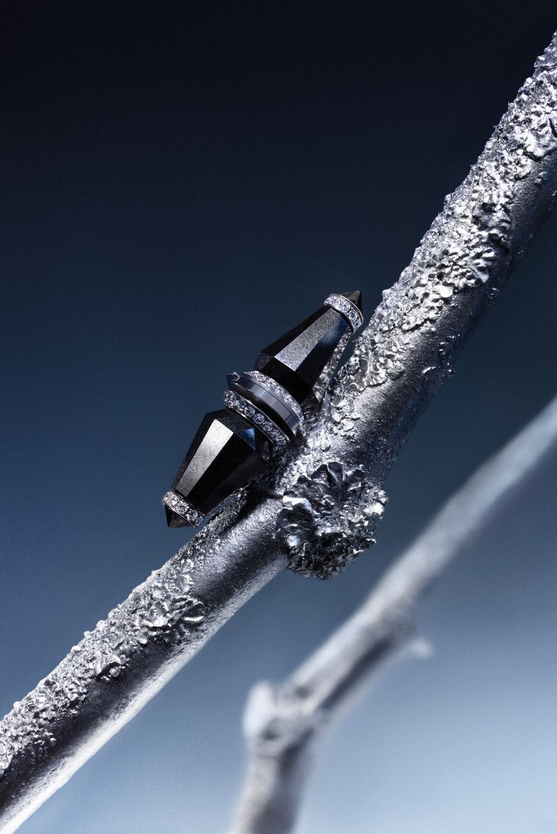 Close-up of black gemstone jewelry set on a textured silver branch against a gradient dark blue background in vertical format.