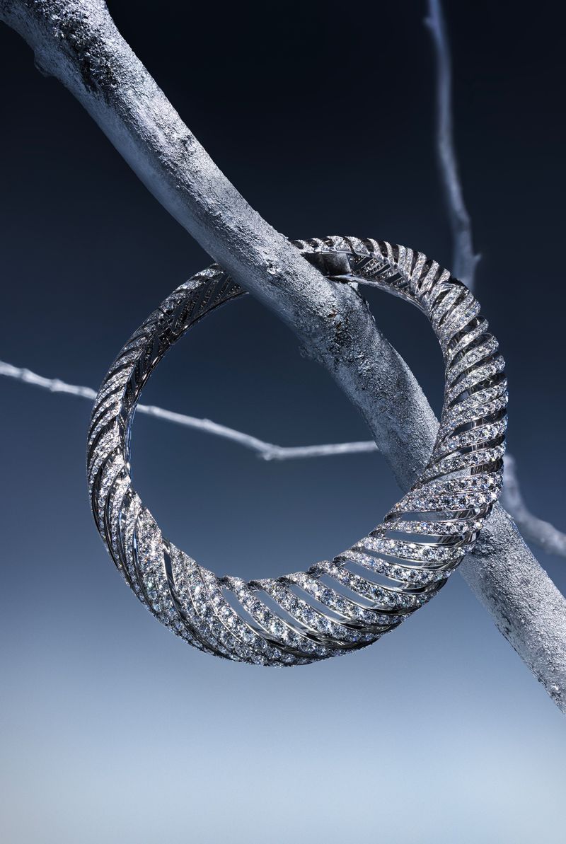 Elegant bracelet encircles a silver-painted branch against a gradient blue backdrop, showcasing its textured, glittering design and unique setting.