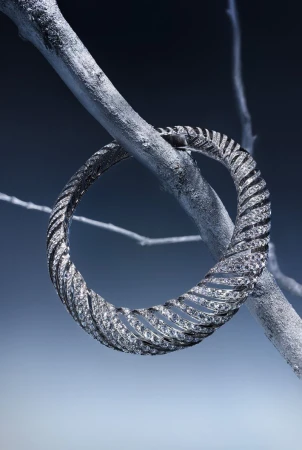 Elegant bracelet encircles a silver-painted branch against a gradient blue backdrop, showcasing its textured, glittering design and unique setting.