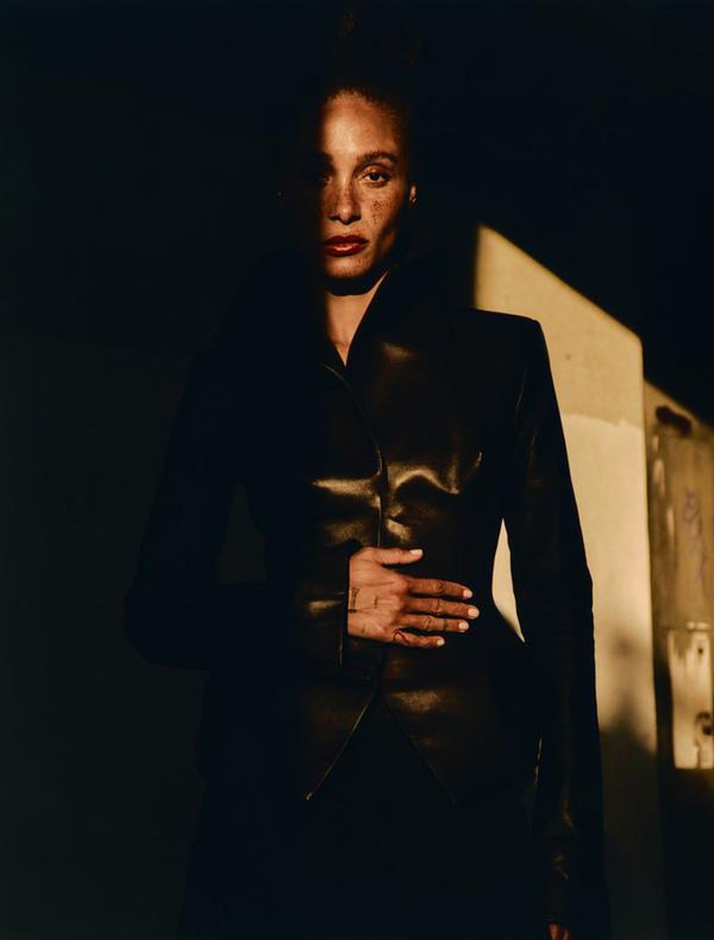 Portrait of a stylish adult woman with freckles wearing a black leather jacket in dramatic, partially-lit indoor environment. 