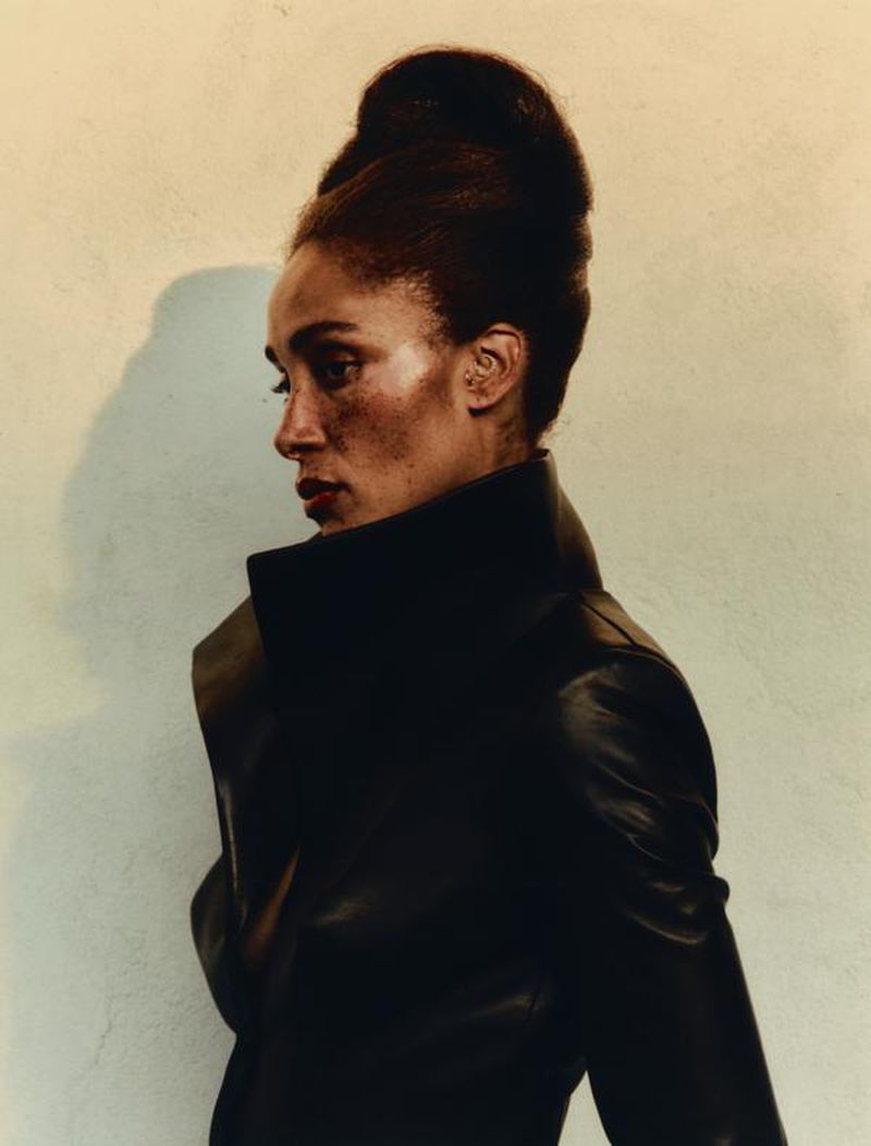 Side profile portrait of a stylish woman with high-volume updo hairstyle and black leather jacket against a neutral backdrop.