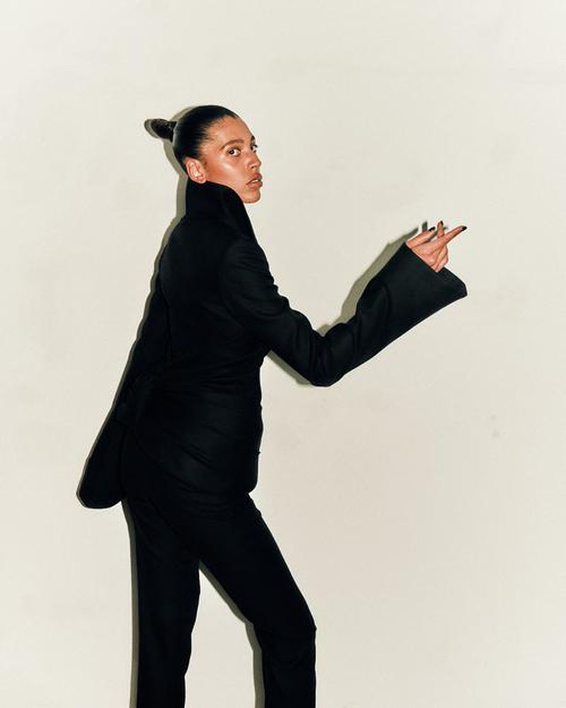 Woman in black suit points with middle finger on white background. Elegant business style, dark hair updo, studio shot.