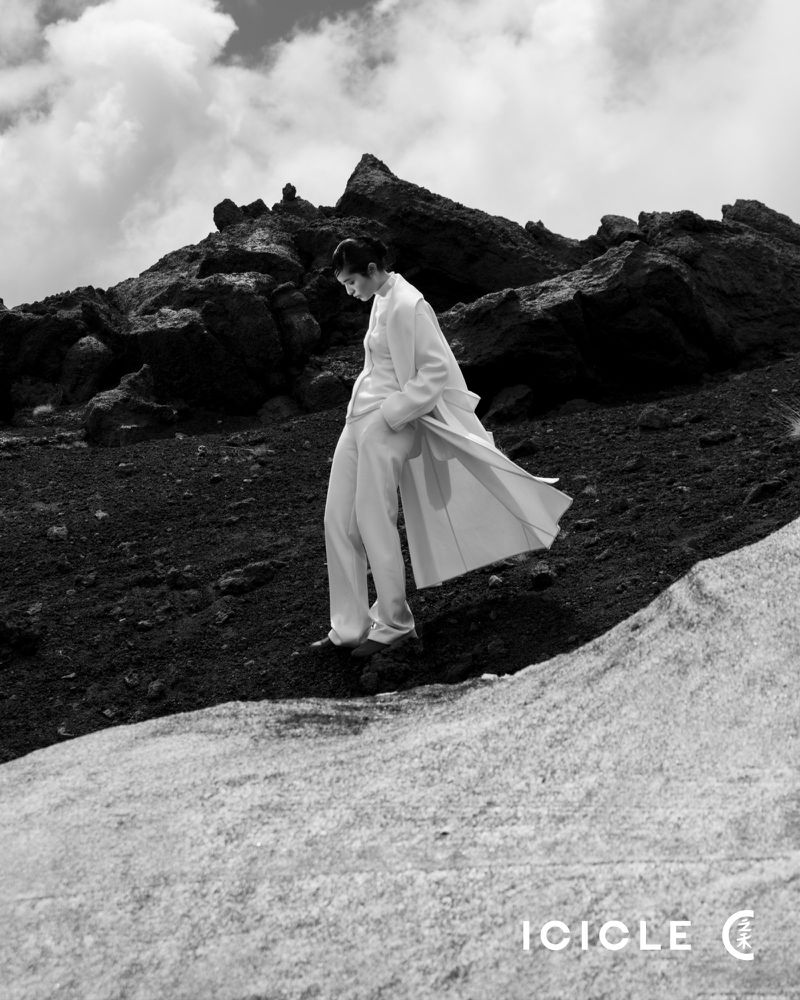 Woman in white coat walks on rocky mountain in black and white with clouds, fashion shot, outdoor, cloudy sky and horizon.