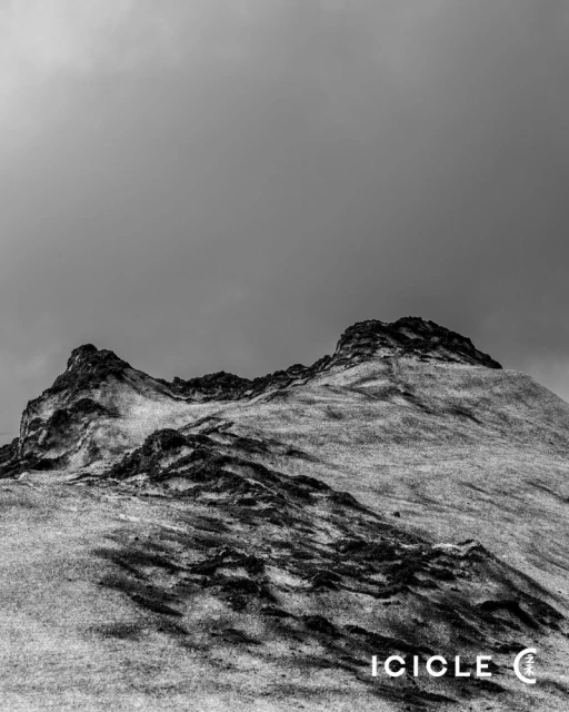 Monochromatic landscape featuring a hillside beneath a cloudy sky, capturing nature's rugged terrain and simple beauty in grayscale.