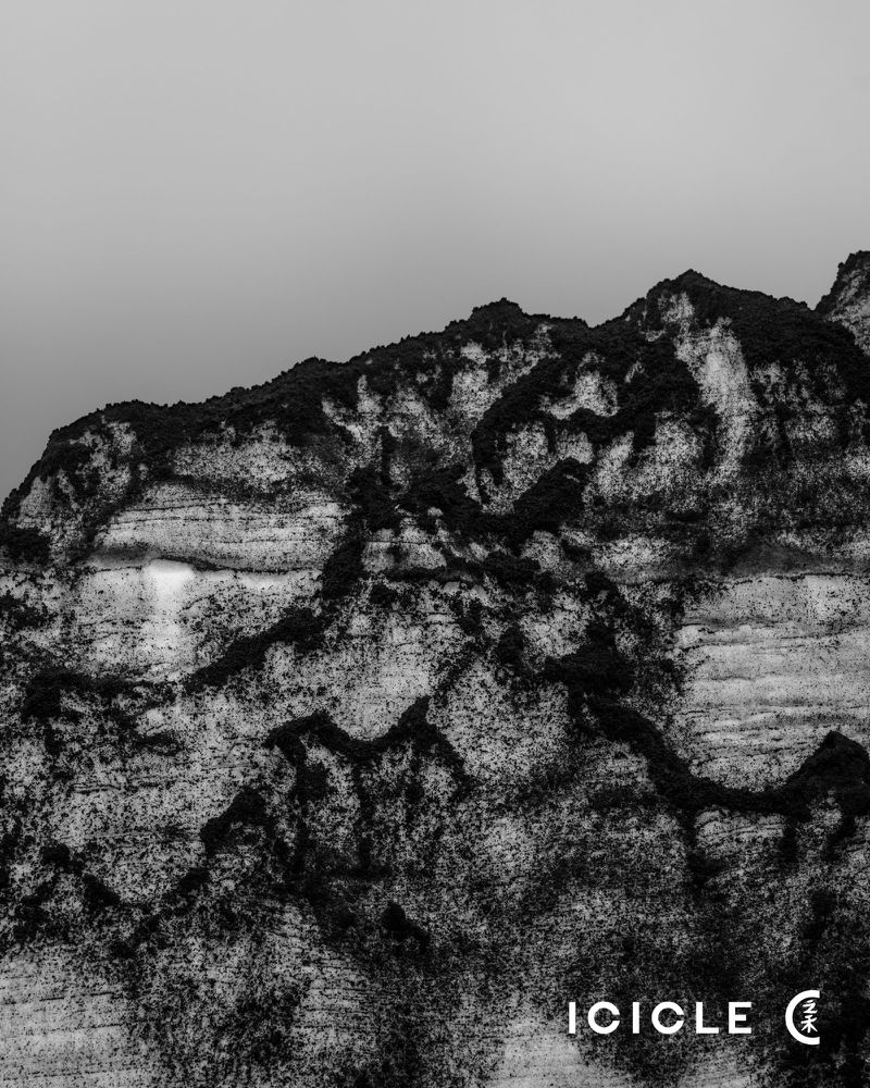 Monochromatic photograph of a rocky mountain against a pale sky, showcasing rugged terrain and textured rock formations.