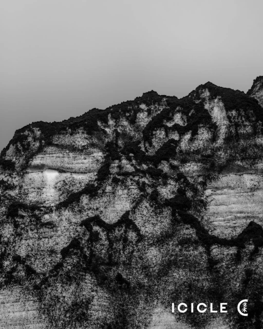 Monochromatic photograph of a rocky mountain against a pale sky, showcasing rugged terrain and textured rock formations.