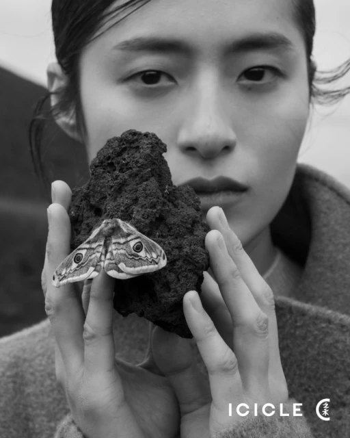 Monochrome image of a woman holding a rock with a moth, showcasing her face and fashion details.