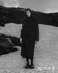 Model wearing a black hooded coat standing on a snow-dusted rocky mountain slope for ICICLE's Water Ink campaign.