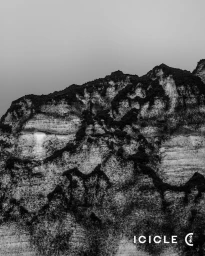 Black and white landscape photograph showing a rugged textured rock cliff face under a muted sky with the ICICLE logo in the corner.