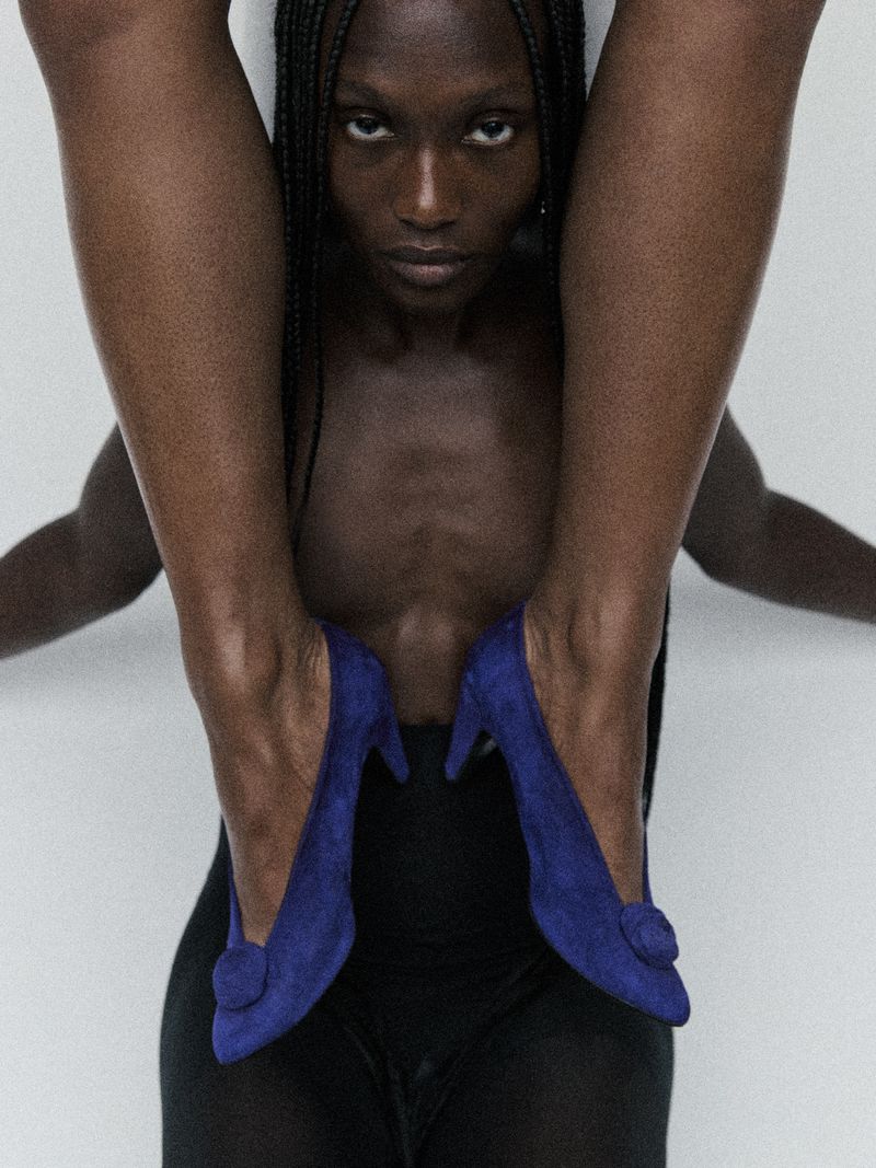 A striking fashion-style shot featuring an African American woman with braids, blue high heel shoes, and a minimalist white backdrop.