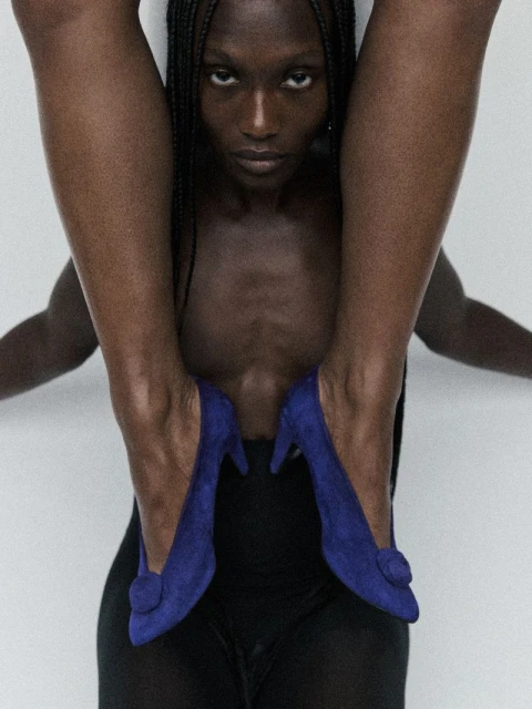 A striking fashion-style shot featuring an African American woman with braids, blue high heel shoes, and a minimalist white backdrop.