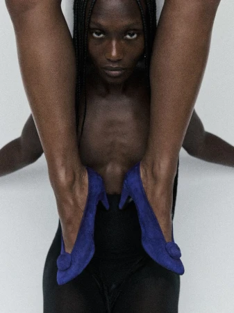 A striking fashion-style shot featuring an African American woman with braids, blue high heel shoes, and a minimalist white backdrop.