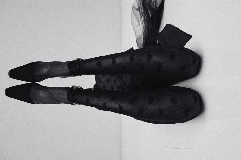 Black and white fashion shot: legs of a woman wearing heart-patterned tights and black high heels, sitting on a tufted ottoman.