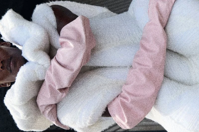 Close-up studio portrait of a woman wearing a puffy white coat and pink sleeves, showcasing fashion, and texture.