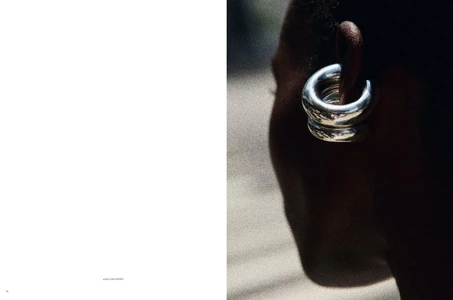 Close-up of a model wearing chunky stacked silver hoop earrings against a dark background in an editorial spread.